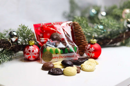 A bag of chocolate Christmas stocking fillers displayed with holiday decorations around it, including Christmas trees and ornaments.