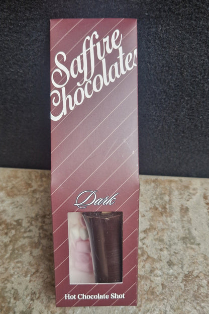 A boxed chocolate product labeled 'Saffire Chocolate' and 'Delic' with a small window showing a dark chocolate stick, placed on a split black and beige textured surface.
