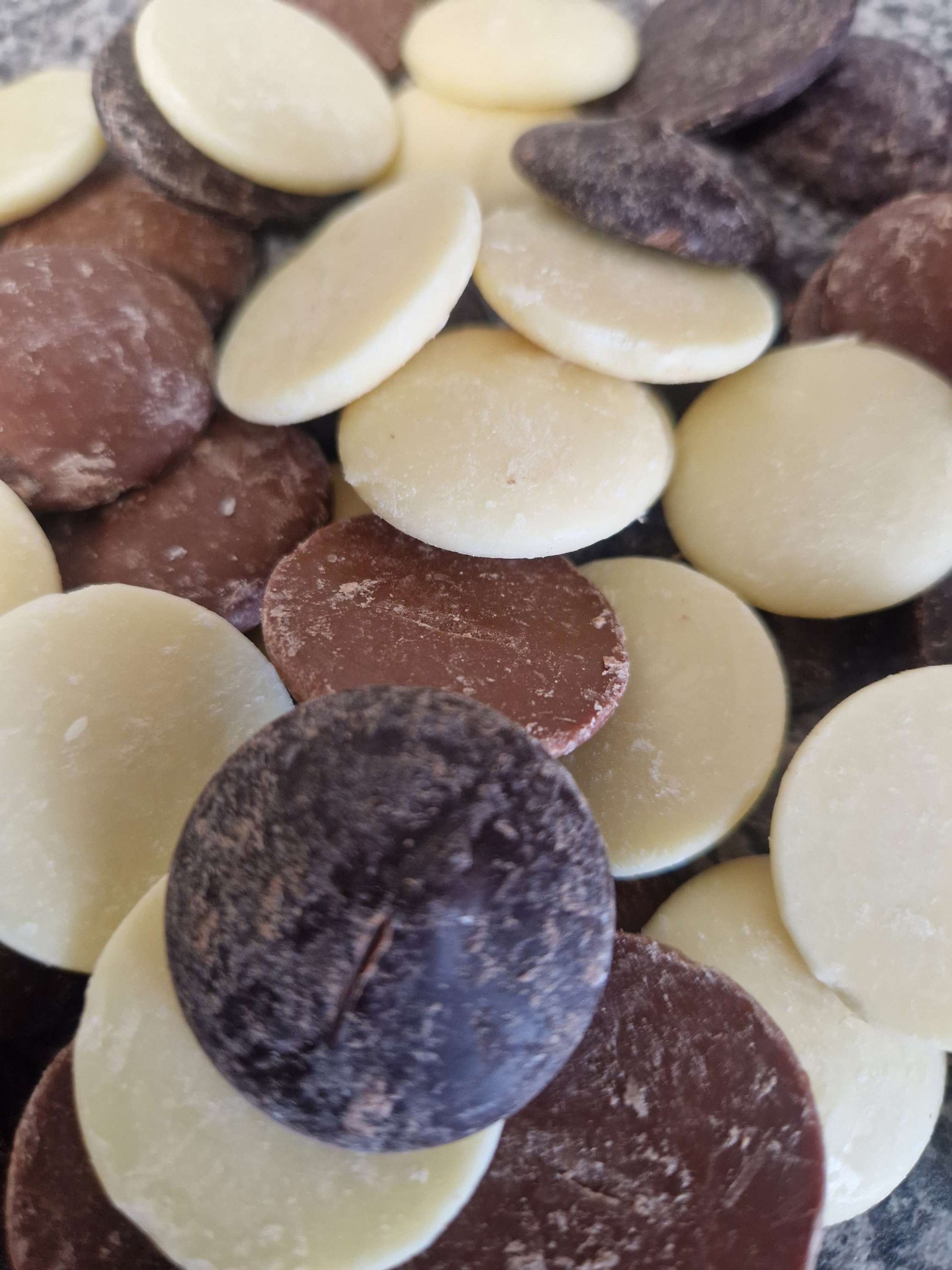 A variety of round Belgium chocolate buttons in white, milk, and dark chocolate colors.