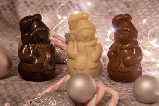 A collection of chocolate snowmen in various colors, with one dark chocolate snowman standing in front of a light background, surrounded by candy canes and pearls.